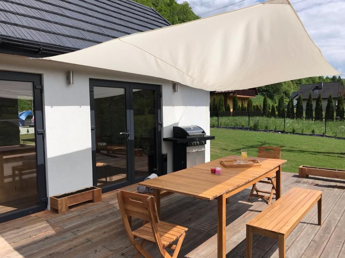Stół na tarasie pod żaglem przeciwsłonecznym, obok grill
